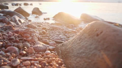 Golden sunset casting warm glowing rays across the rocky shoreline Stock Footage 337416424