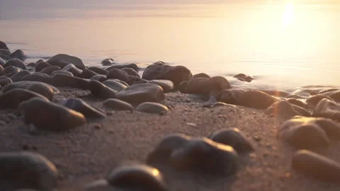 Golden sunset casting warm light over smooth pebbles on shore Stock Footage 337418255
