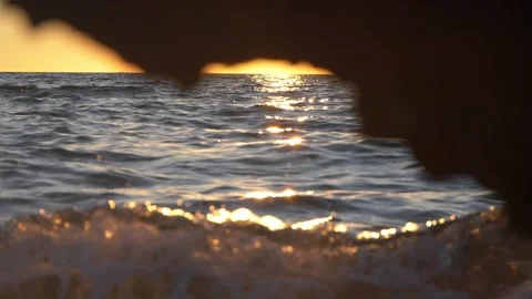 Golden sunset framed by dark rocks overlooking the sparkling ocean. Stock Footage 337408644