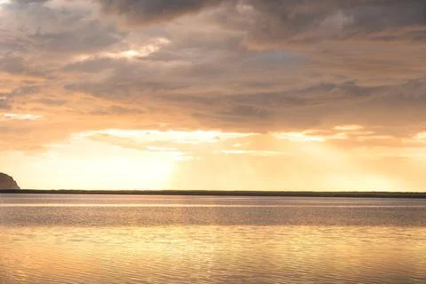 Golden sunset illuminates dramatic clouds above calm water in Iceland Fotos Stock
