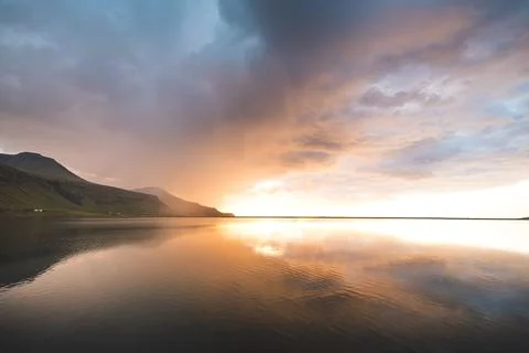 Golden sunset illuminates dramatic clouds above calm water in Iceland Фото