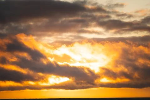 Golden sunset illuminates dramatic clouds above calm water in Iceland Fotos Stock