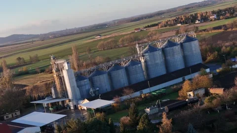 Golden sunset illuminates metallic grain silos in a village, surrounded by .. Stock Footage 258334608