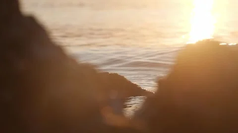 Golden sunset light glowing over calm ocean through rocky foreground Stock Footage 337405022