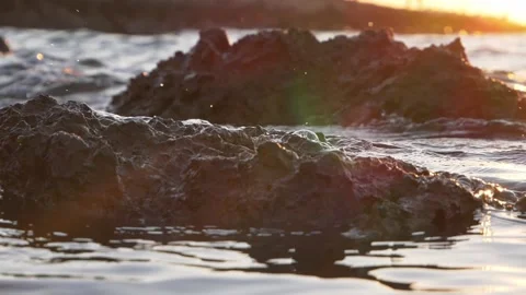 Golden sunset light illuminates dark rocky coast during ocean tide Stock Footage 337411083
