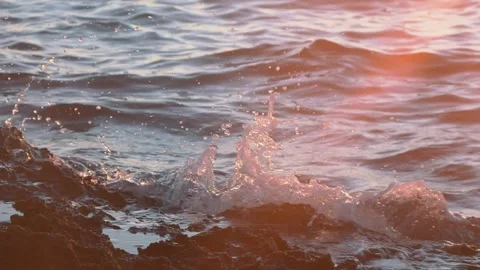 Golden sunset light illuminates ocean waves splashing against rocky shore Stock Footage 337409191