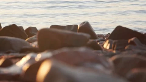 Golden sunset light illuminates smooth rocks along calm coastal beach Stock Footage 337410731