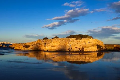 Golden sunset light illuminating a dramatic coastal rock formation reflected in  Stock Photos