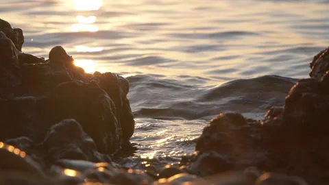 Golden sunset light reflecting on calm ocean water between rocks Stock Footage 337405096