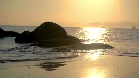 Golden sunset light reflecting on ocean waves at a peaceful rocky beach Stock Footage 342214484