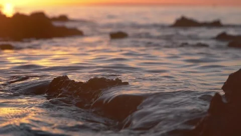 Golden sunset light reflects on serene ocean waves near rocks Stock Footage 337410438