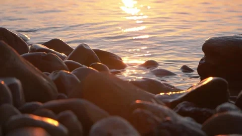 Golden sunset light reflects on smooth rocks along calm shore Stock Footage 337410867