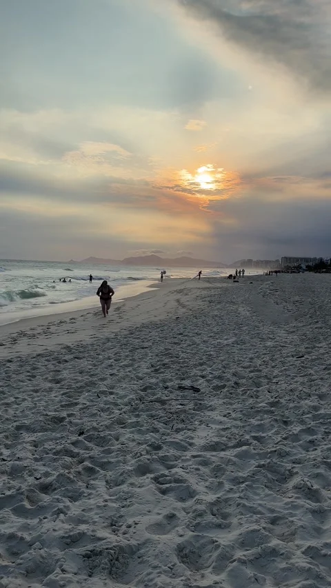 Golden sunset at ocean beach with waves and relaxing visitors as a woman emerges 库存影片 333143163