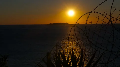 Golden sunset over ocean behind barbed wire fence Stock Footage 302822517
