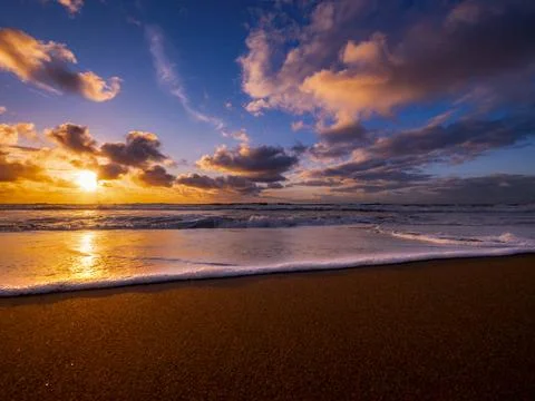 Golden sunset over the ocean with dramatic clouds and gentle waves on the sho Foto stock