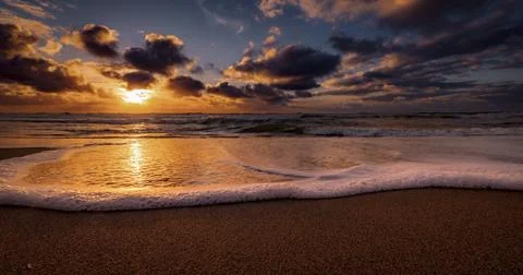 Golden sunset over the ocean with dramatic clouds and gentle waves lapping .. Foto stock