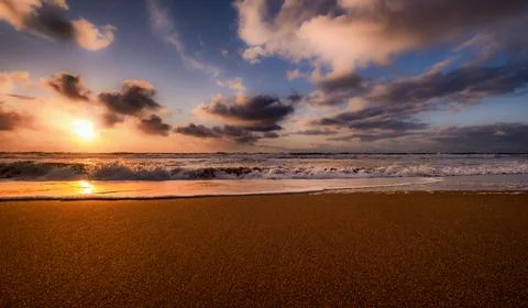 Golden sunset over the ocean with dramatic clouds and gentle waves on the sho Foto stock