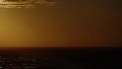 Golden sunset over a tranquil ocean, gentle waves shimmering as the low sun Stock Footage 316779687