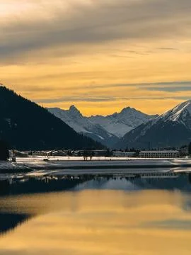 Golden sunset reflecting on snowy mountain lake with buildings Foto stock
