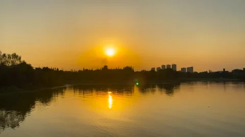 Golden sunset reflection on calm lake water with distant city skyline at dusk Stock Footage 342333228