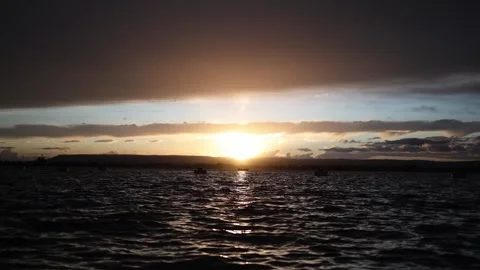 Golden sunset reflections over dark moving water beneath dramatic layered clouds Stock Footage 328286564