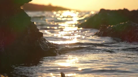 Golden sunset shimmers through dark coastal rocks on ocean waves. Stock Footage 337406711