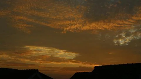 Golden sunset sky with clouds over silhouette of house roofs Stock Photos