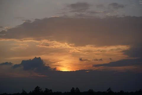 Golden sunset sky with dramatic clouds over a dark horizon at dusk Stock Photos