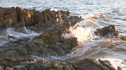 Golden sunset waves crash dramatically against rugged coastal rock formations Stock Footage 337409077