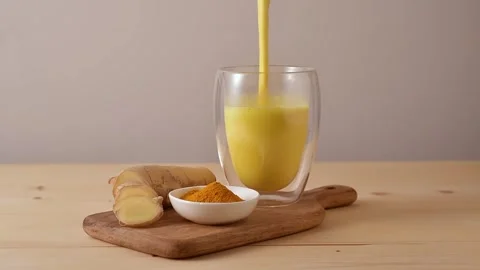 Golden turmeric latte being poured into a clear glass, fresh ginger root and Stock Footage 313634853