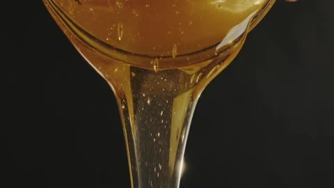 Golden viscous bee honey flows from a glass container in slow motion against Stock Footage 309952048