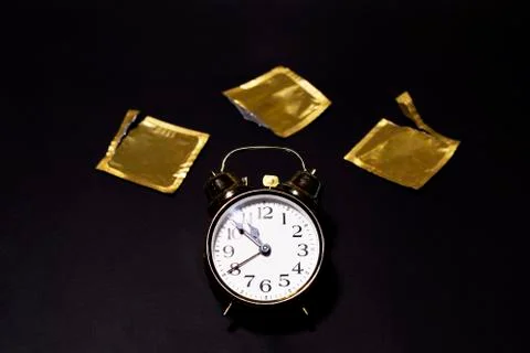 Golden watch is on a black background with opened condoms. Stock Photos