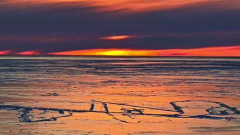 Golden winter sunset reflecting over a tranquil frozen lake with cracked ice Stock Footage 346594507
