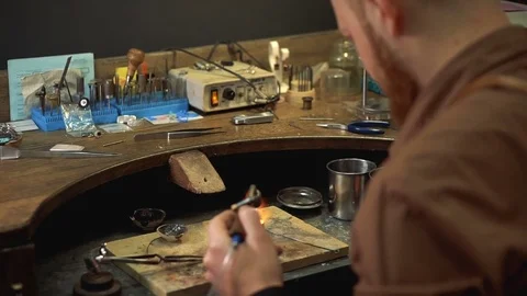 Goldsmith sitting back and holding a soldering by heating mold in the craft room Stock Footage 72965277