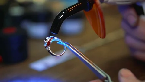 Goldsmith turns the ring and dried enamel on it use an ultraviolet instrument Stock Footage 73813313