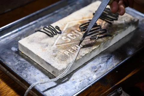 Goldsmith using tweezers is putting a silver chain on a soldering block Stock Photos