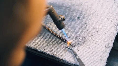 Goldsmith welds decorative chain on fireproof sheet closeup Video stock 120804594