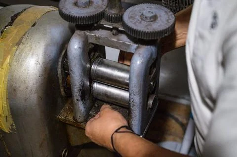 Goldsmith working with a rolling mill shaping metal in his workshop Stock Photos