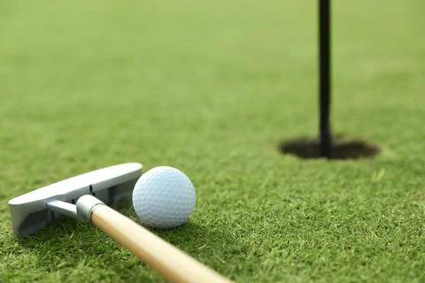 Golf ball and club near hole on green course Stock Photos