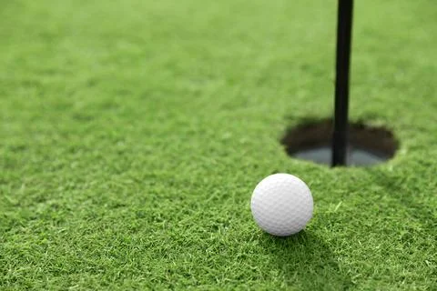 Golf ball near hole on green course, space for text Stock Photos