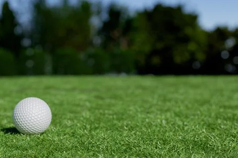 A golf ball rests on a lush green lawn under a clear sky. Stock Illustration