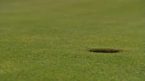 Golf ball rolling from left to drop into close-up hole at right; hand retrieves Stock Footage 59518409