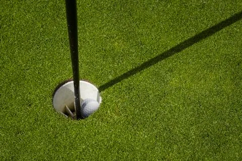Golf ball sit inside cup on golf course putting green with flag Stock Photos