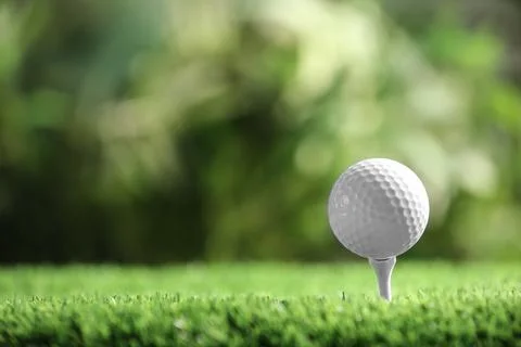 Golf ball with tee on artificial grass against blurred background, space for  Photos