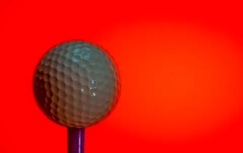 Golf ball on tee peg ready to play. Red background Stock Photos