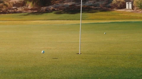 Golf balls rolling toward the flagstick on a desert putting green at golden hour Vídeos de archivo 340117519