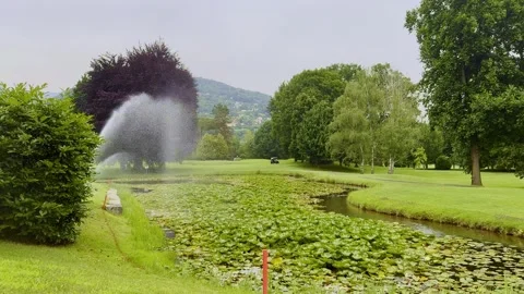 Golf Course in the Mountain with a Pond and Water Sprinkler Stock Footage 244635048