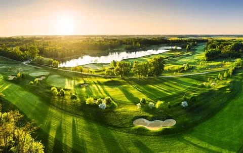 Golf course panorama at dramatic sunrise with green fairways and forest Stock Photos