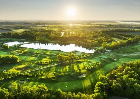 Golf course panorama at dramatic sunrise with green fairways and forest Stock Photos