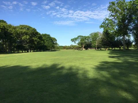 Golf course sunlight tree shadows across the fairway Stock Photos